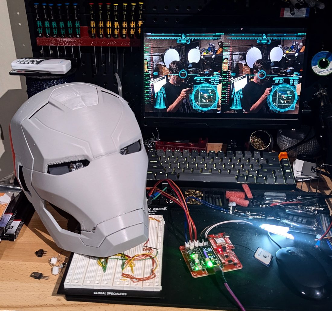 A 3D-printed Iron Man helmet on the workbench next to the electronics and HUD